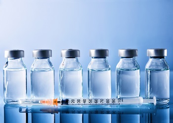 Row of vials with medication and syringe on blue methacrylate table.