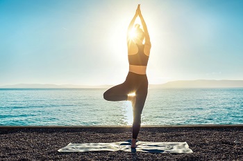 Image of yoga inspiration on nature.  Silhouette of person doing yoga pose against a sunset on the ocean.