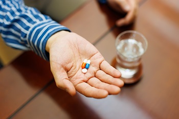 View of a man holding pills in hand with a glass of water nearby.